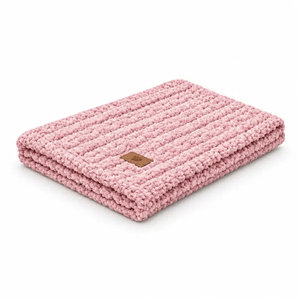 A folded pink chunky knit blanket with a small brown leather brand patch, shown on a solid white background.