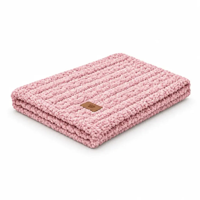 A folded pink chunky knit blanket with a small brown leather brand patch, shown on a solid white background.