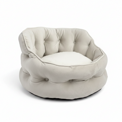 A tufted round pet bed in a light cream or off-white fabric, shown from the front on a white circular base against a solid green background.