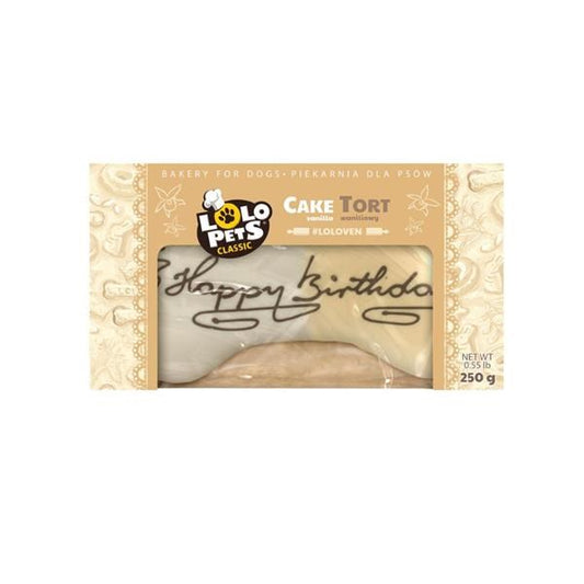 A packaged dog treat bone from Polo Pets Classic, specifically the 'Cake Tort' flavor. The bone is visible through a clear window in the packaging, which features a beige and gold patterned design with 'Happy birthday' written in black script across the front.