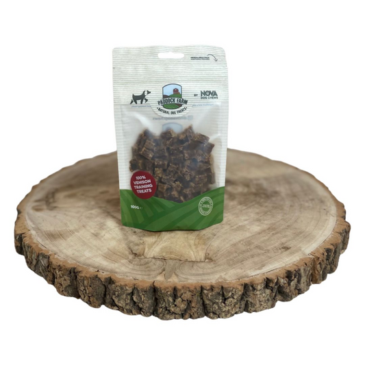 A stand-up pouch of dog training treats placed on a round natural wood slice tray against a plain white background. The package appears to be Nova Farm dog treats, with the brand logo and product window visible.